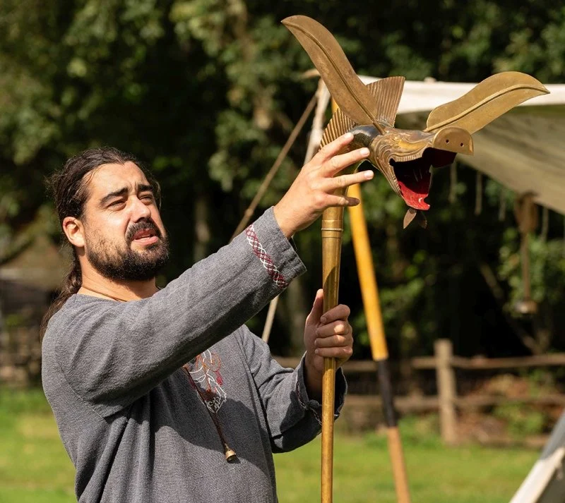 A man dressed in Saxon era clothing demonstrates how to play a carnyx