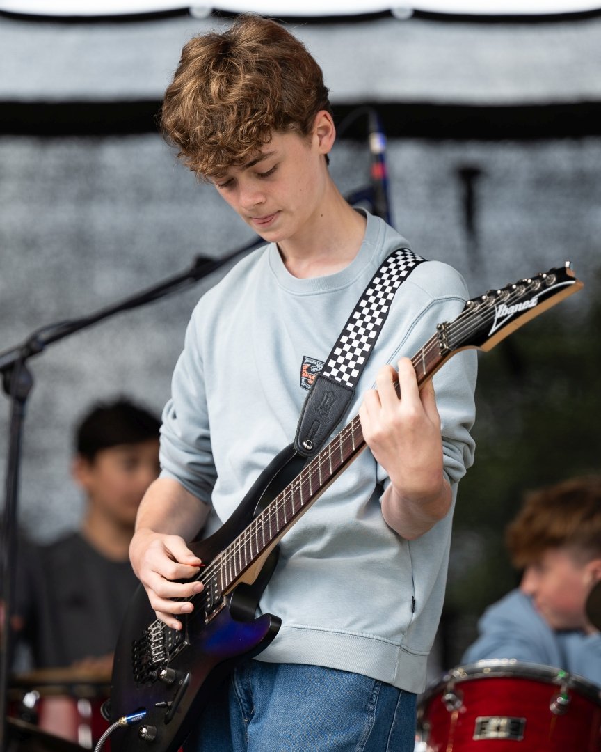A teenage boy plays guitar on stage