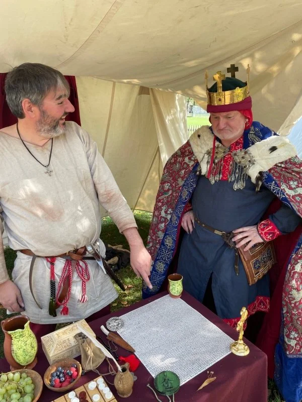 A re-enactor dressed as Kind John does not look impressed when another re-enactor points at a historical document