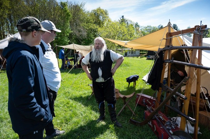 A family talking to a re-enactor dressed in Tudor period costume in an encampment