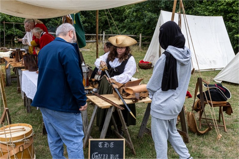 People watching a re-enactor demonstrate 18th century weapons in a living history camp