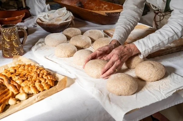 Hands place a ball of dough next to other round balls of dough on a wooden board covered with muslin