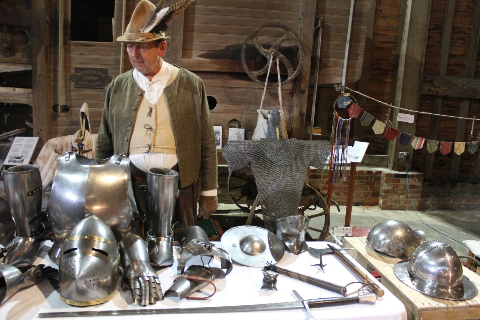A man dressed in Tudor period costume stands behind a table full of Tudor armour