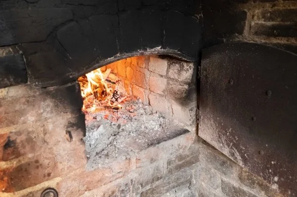 The door of a brick built bread oven is open showing us the fire inside