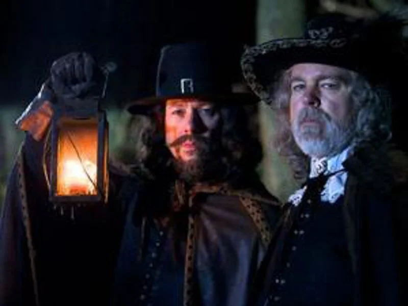 two men dressed in costumes from the Stuart period holding a lantern