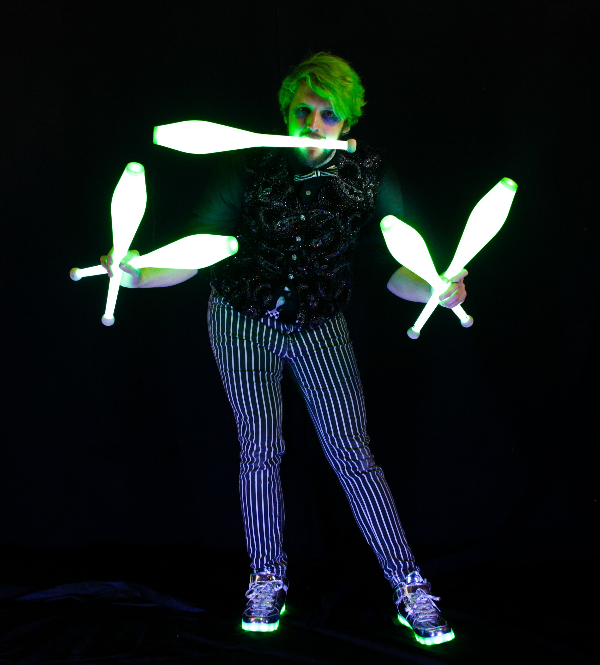 A man dressed as the Joker juggles illuminated clubs