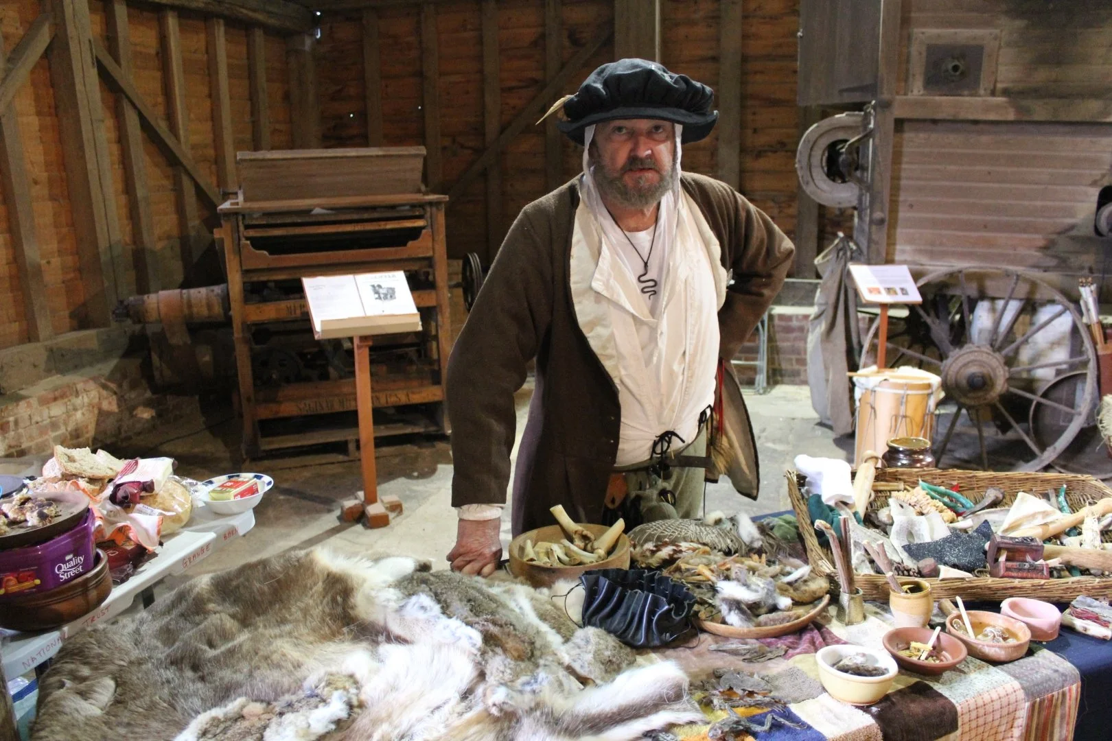 A man dressed in Tudor period costume is standing next to a table of bones and furs
