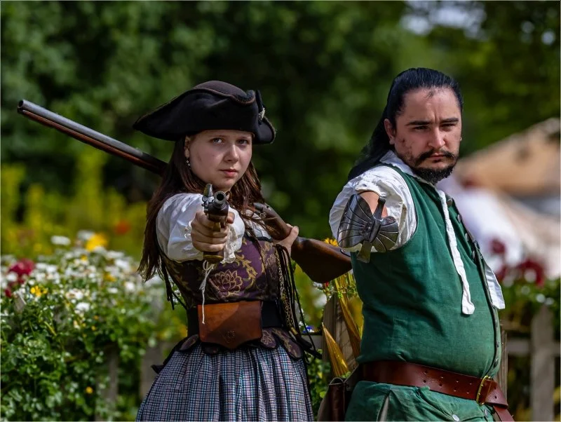 A man and woman dressed as 18th Century highwaymen brandishing weapons at the camera