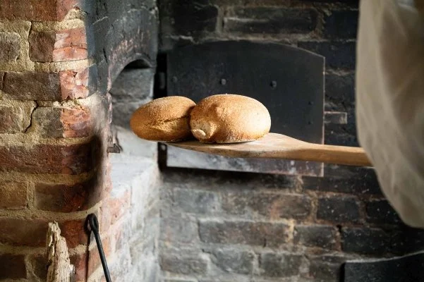 Two freshly baked rolls are being taken out of a brick built oven in an old cottage