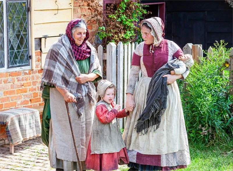 An older lady, a female adult, young girl and baby all dressed in ragged Victorian clothing