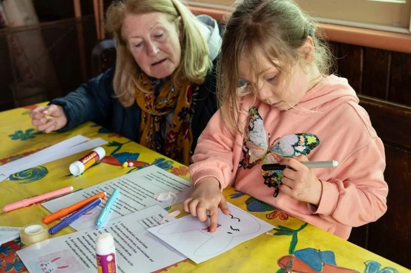 A young girl colouring in a rabbit mask
