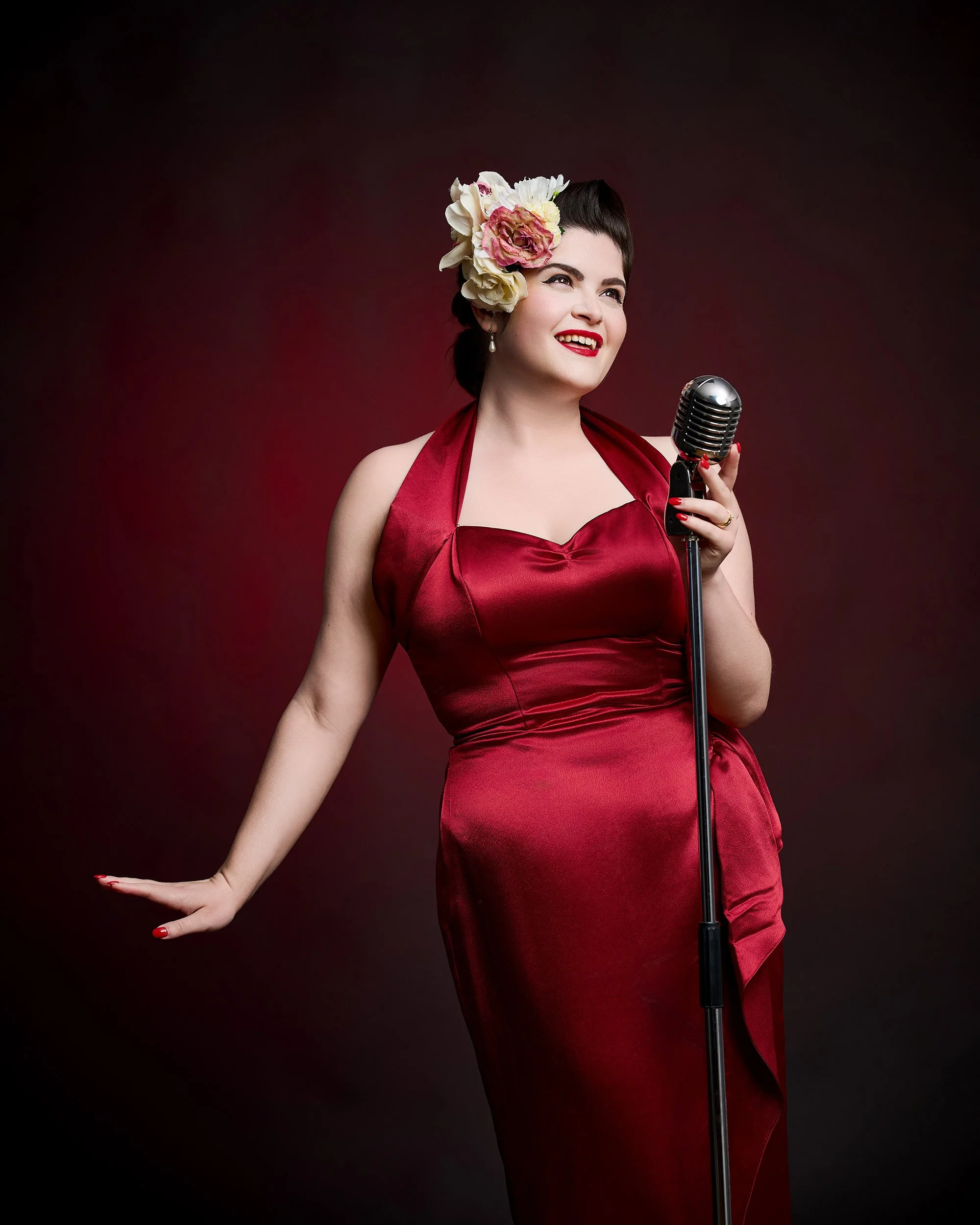 A woman in a red vintage 1940s dress sings into a vintage microphone