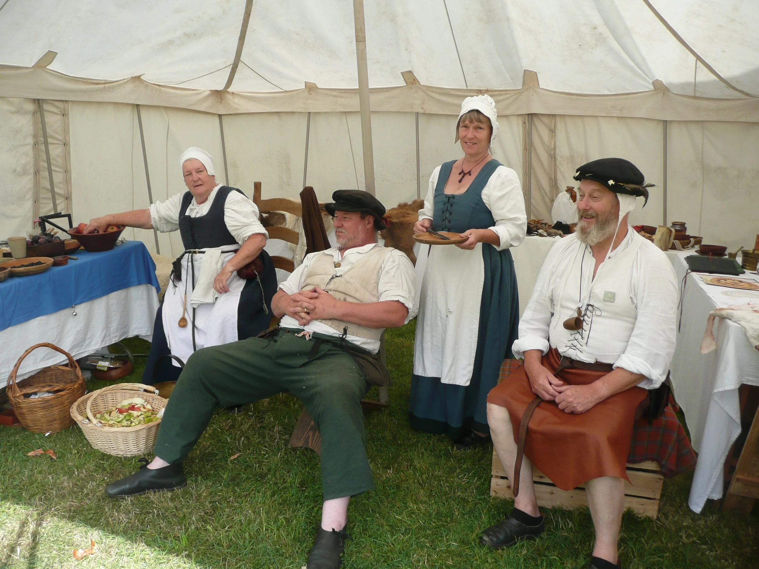 A group of Tudor period re-enactors sit together in a traditional tent, surrounded by objects that represent Tudor life