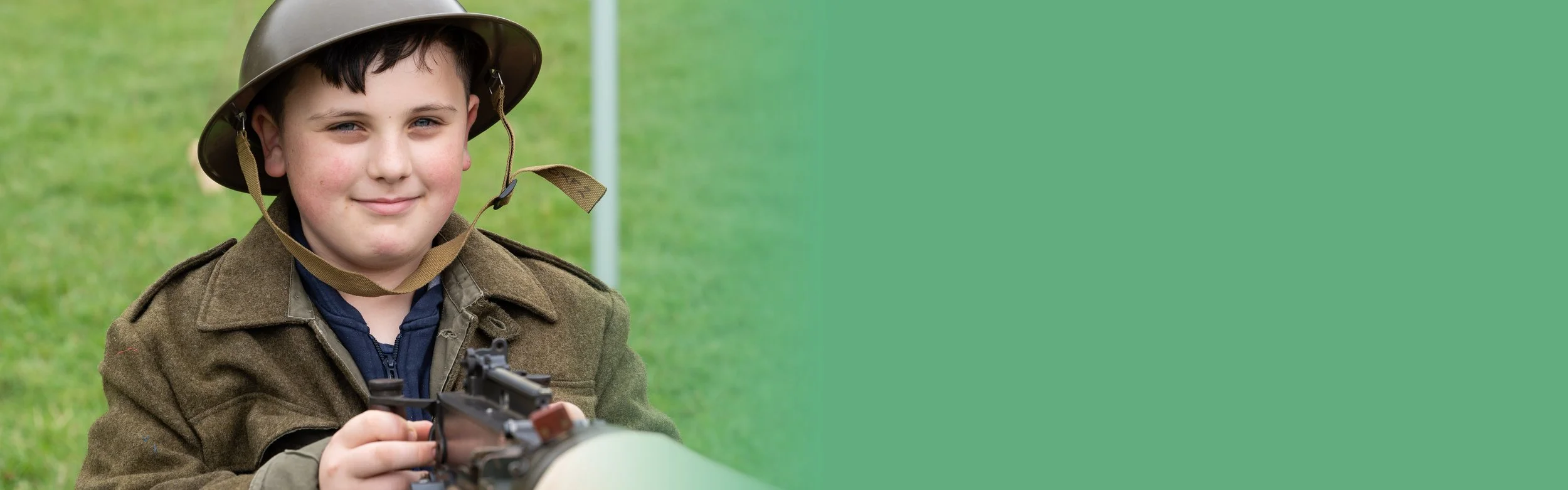 A smiling boy is dressed in WW2 jacket and helmet