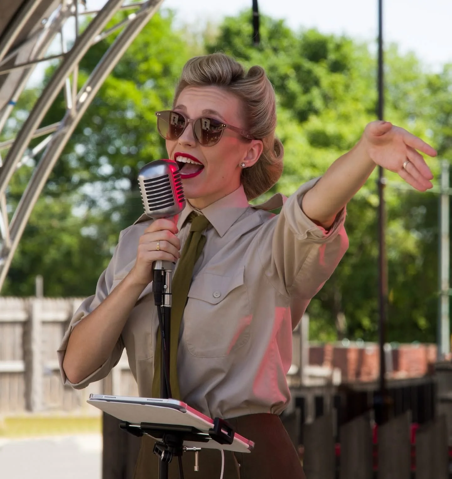 A woman dressed in 1940s shirt and tie is singing with a vintage microphone