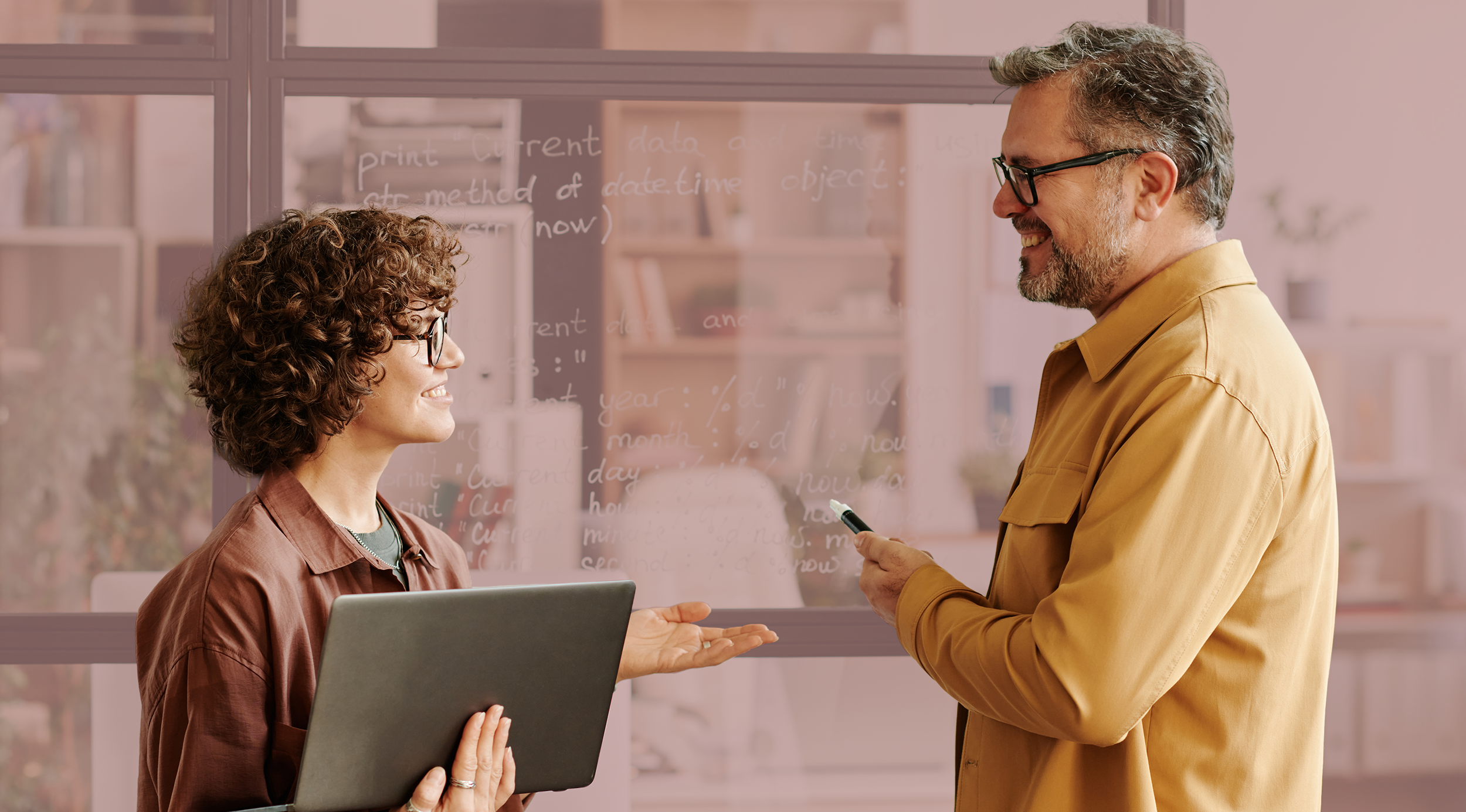 Homem e mulher discutindo em escritório com quadro de vidro ao fundo, onde há anotações em código.