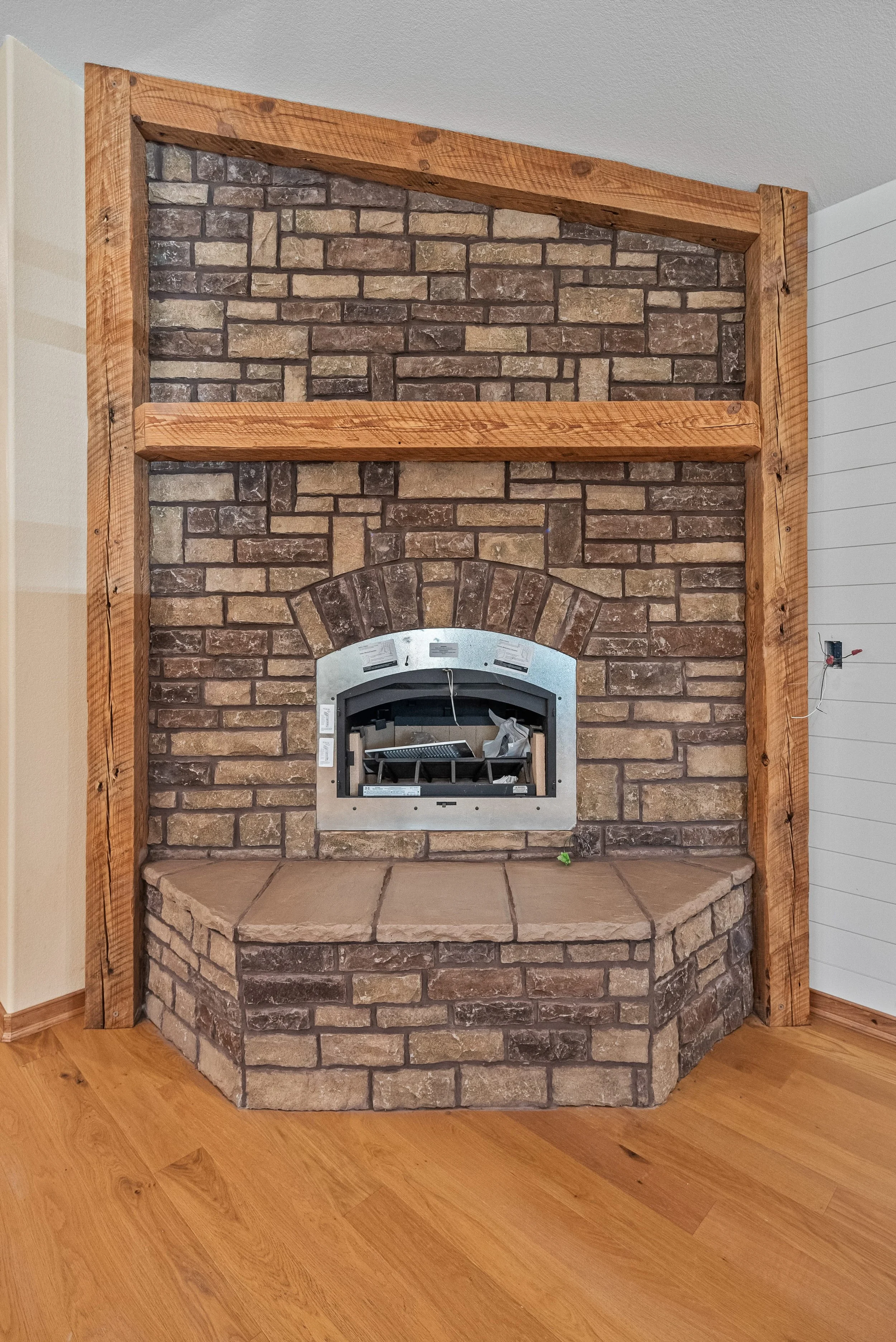 Corner fireplace with brick wall, wooden framing, and a stone hearth in a living room.