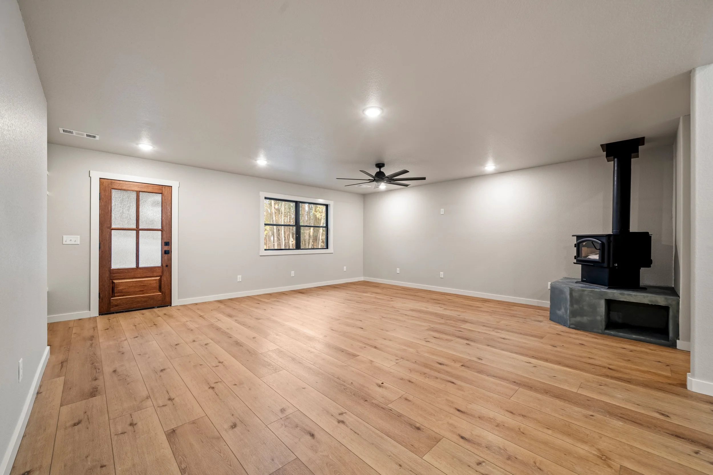 Spacious living room with wood flooring, wood stove, and modern ceiling fan.