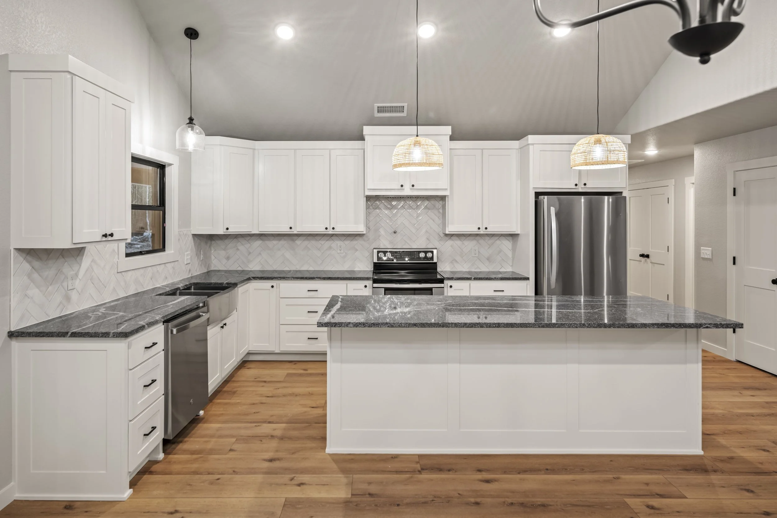Modern kitchen with white cabinets, gray countertops, stainless steel appliances, wooden flooring, and pendant lights.