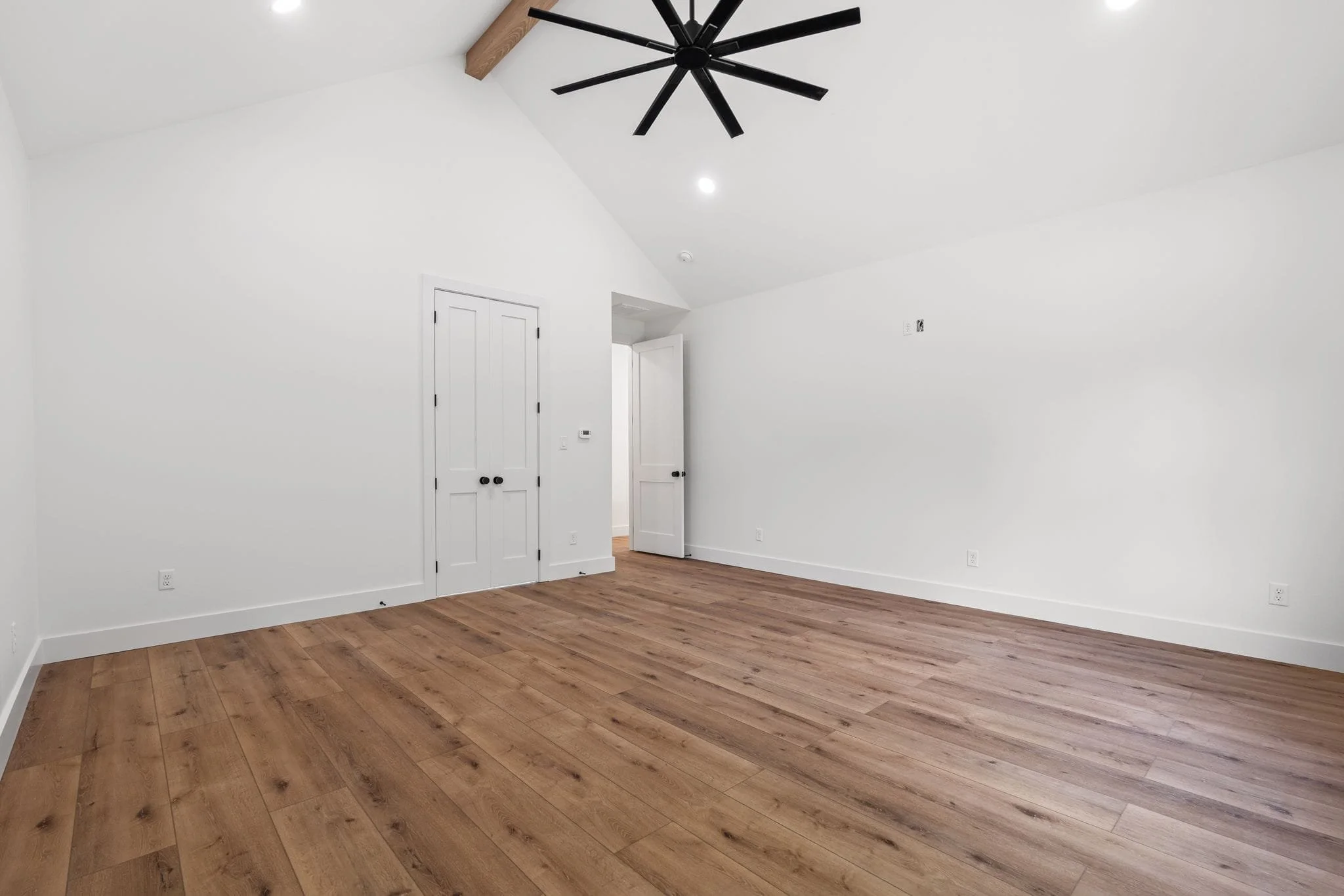Empty room with white walls, wood flooring, a closed closet door, and a ceiling fan with black blades.