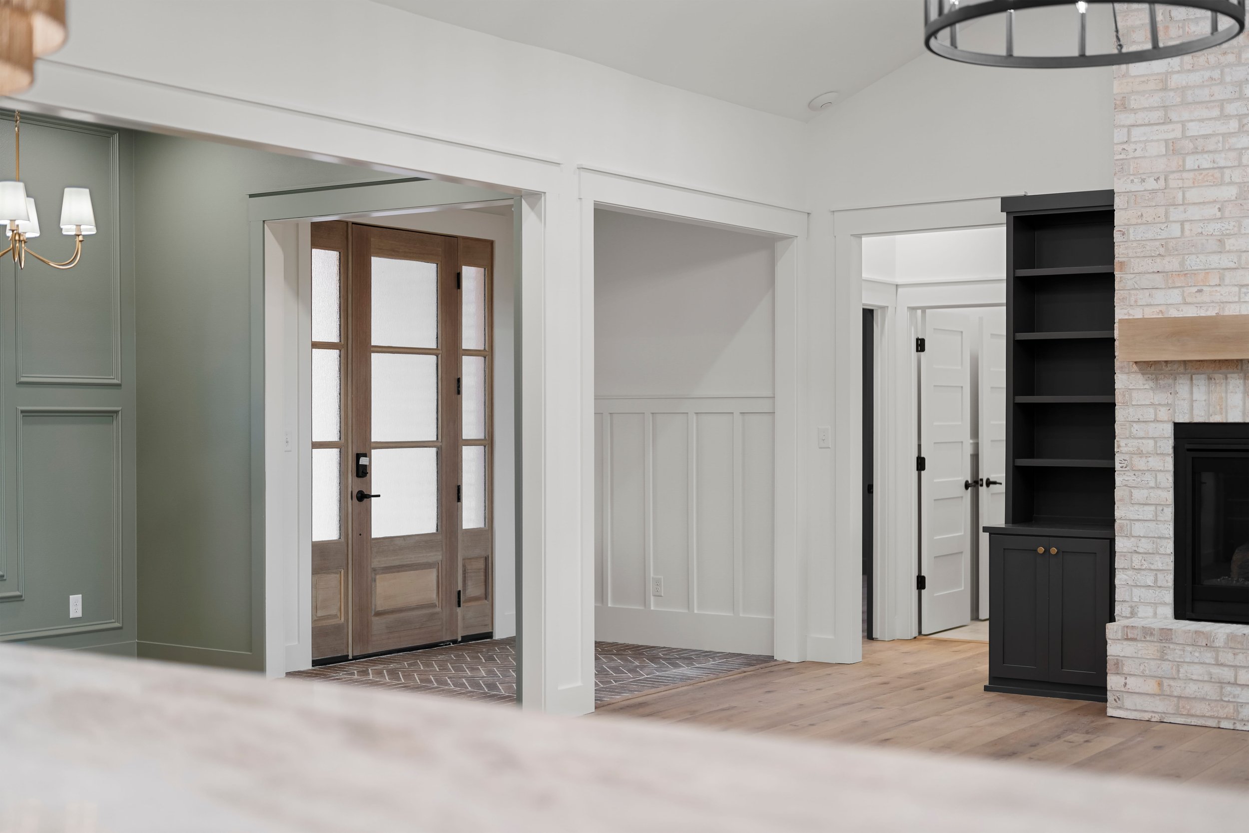 Interior of a modern home with a front door, white walls, and a wood floor, featuring a brick fireplace with a black bookcase beside it.