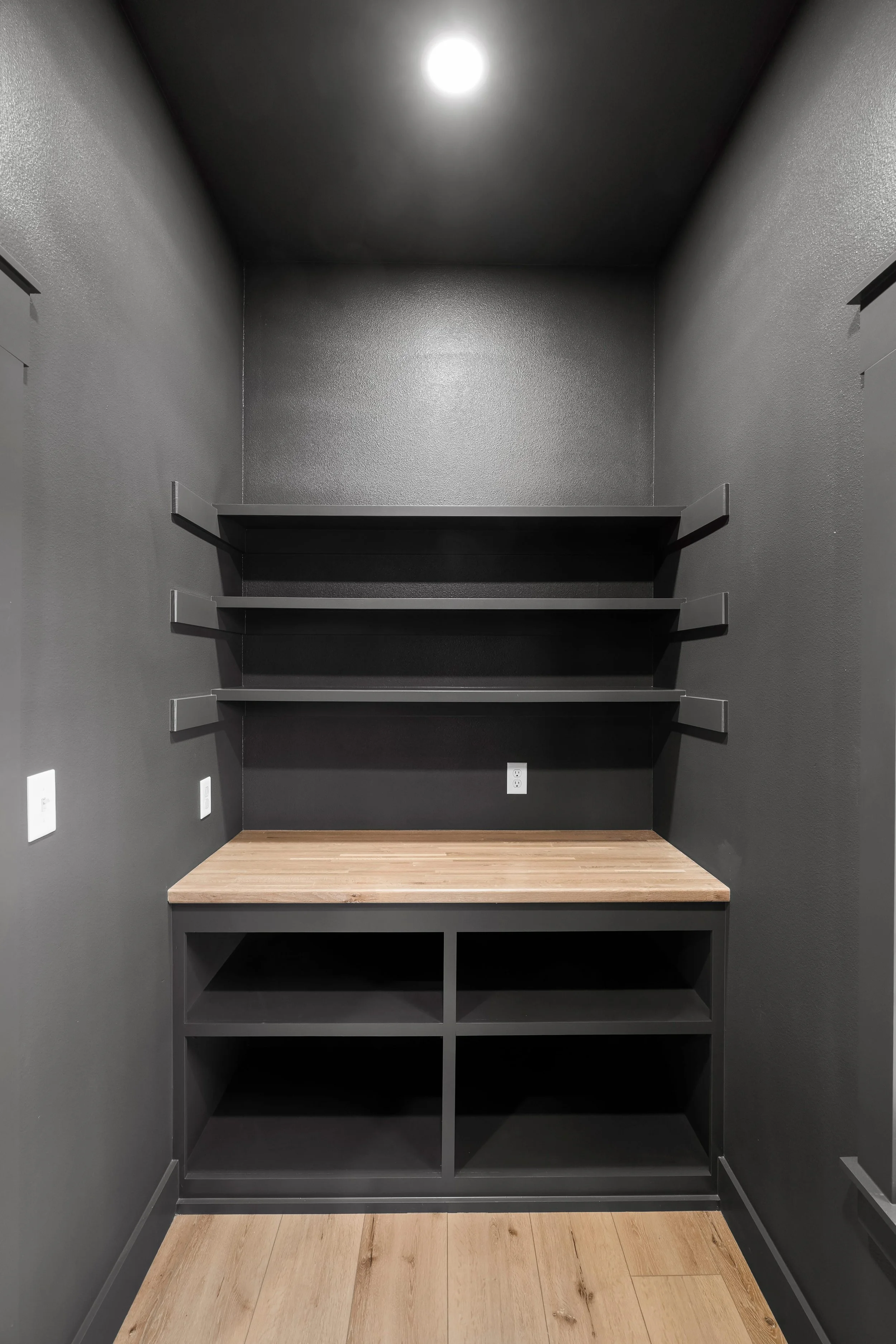 Empty black closet with built-in shelves, a countertop, and cubbyholes at the bottom, with wood flooring and electrical outlets.