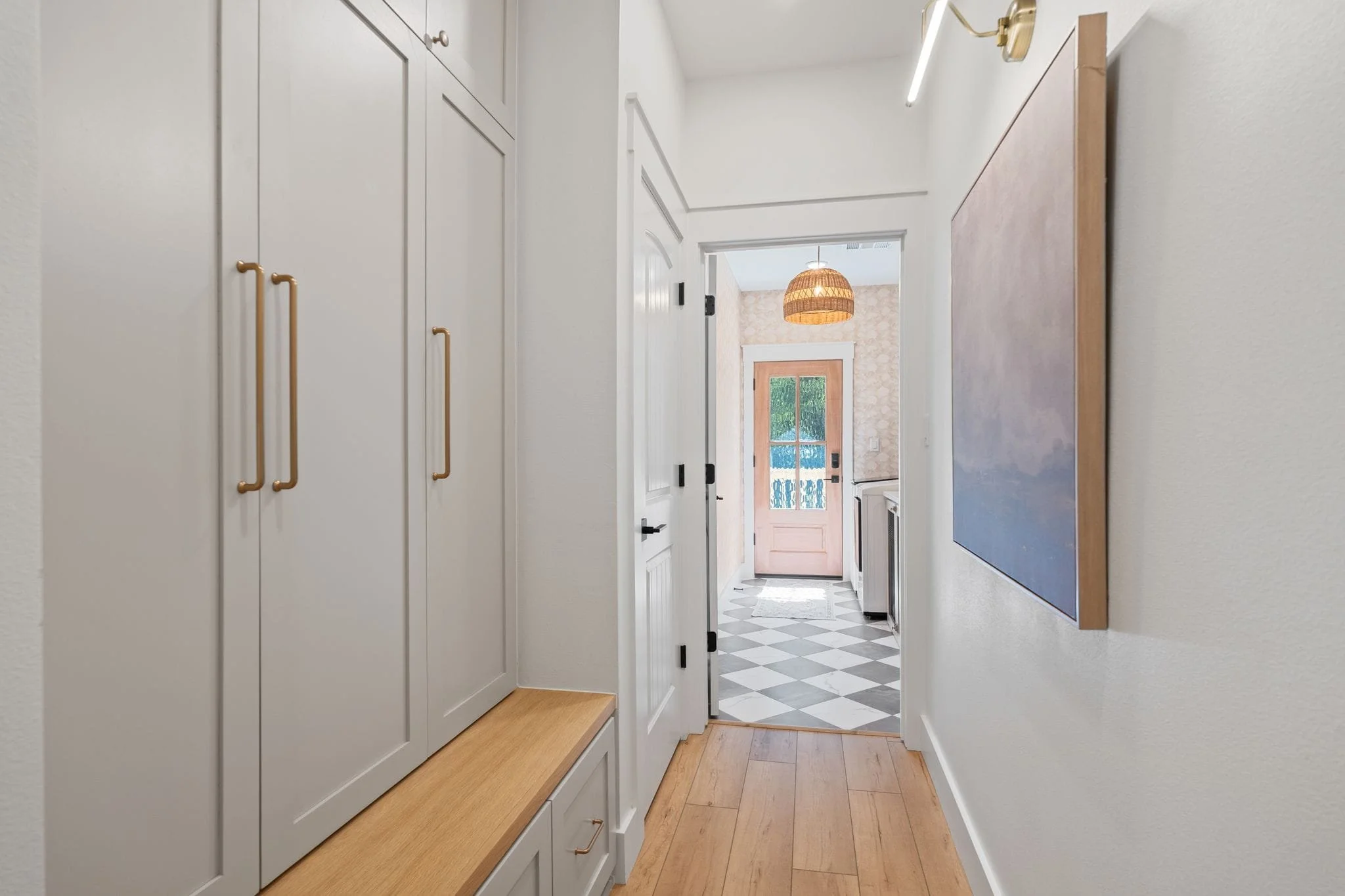 Hallway mudroom area with built-in storage cabinets, bench seating, and view into adjacent laundry room.
