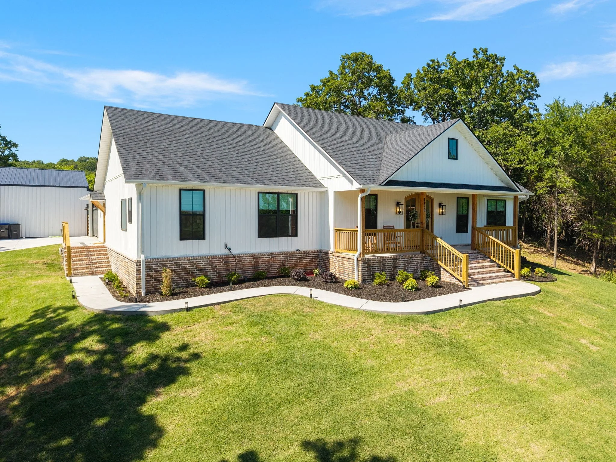 Angled exterior view of white farmhouse with wraparound landscaping and front porch