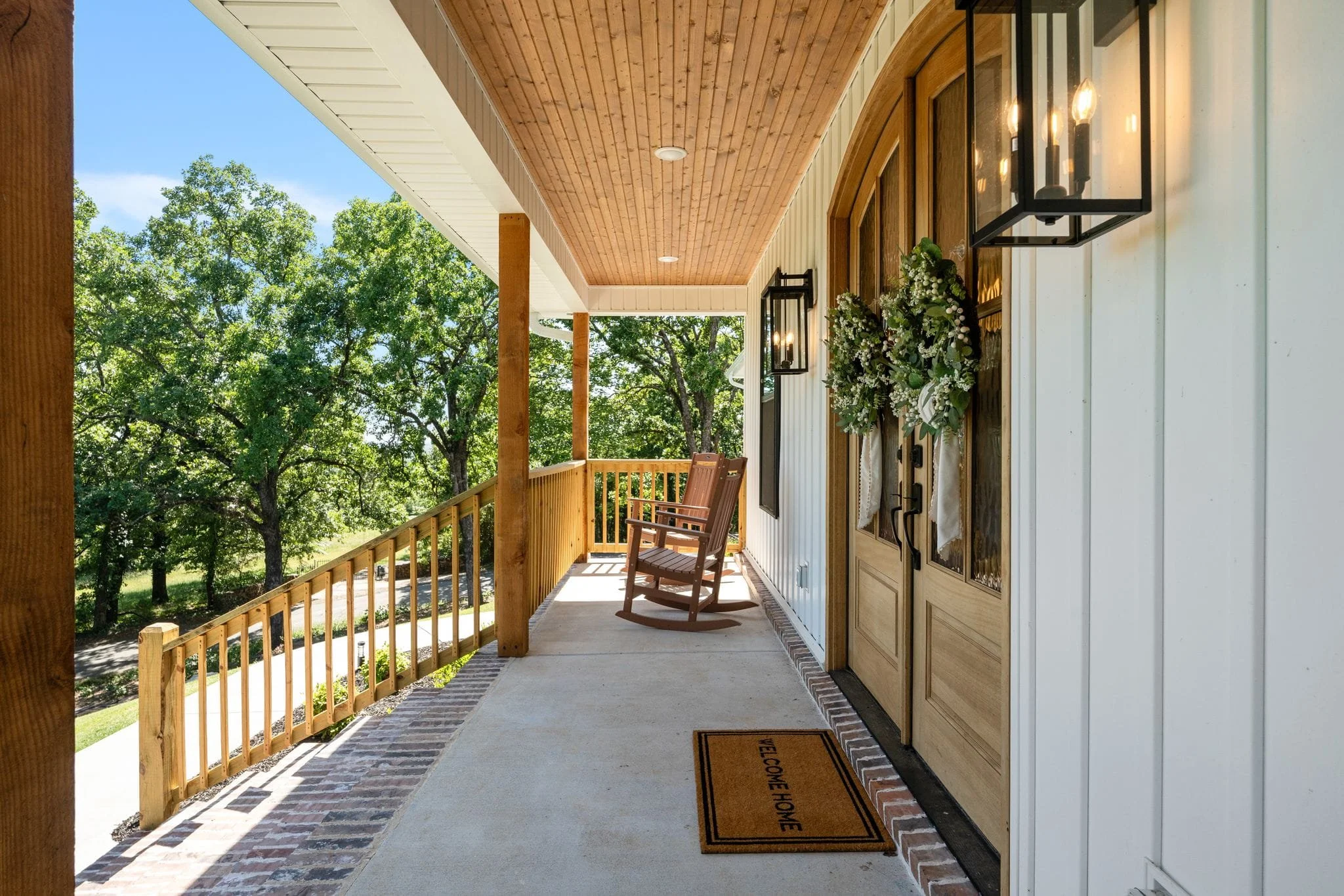 Covered front porch with wood ceiling, rocking chairs, and double entry doors