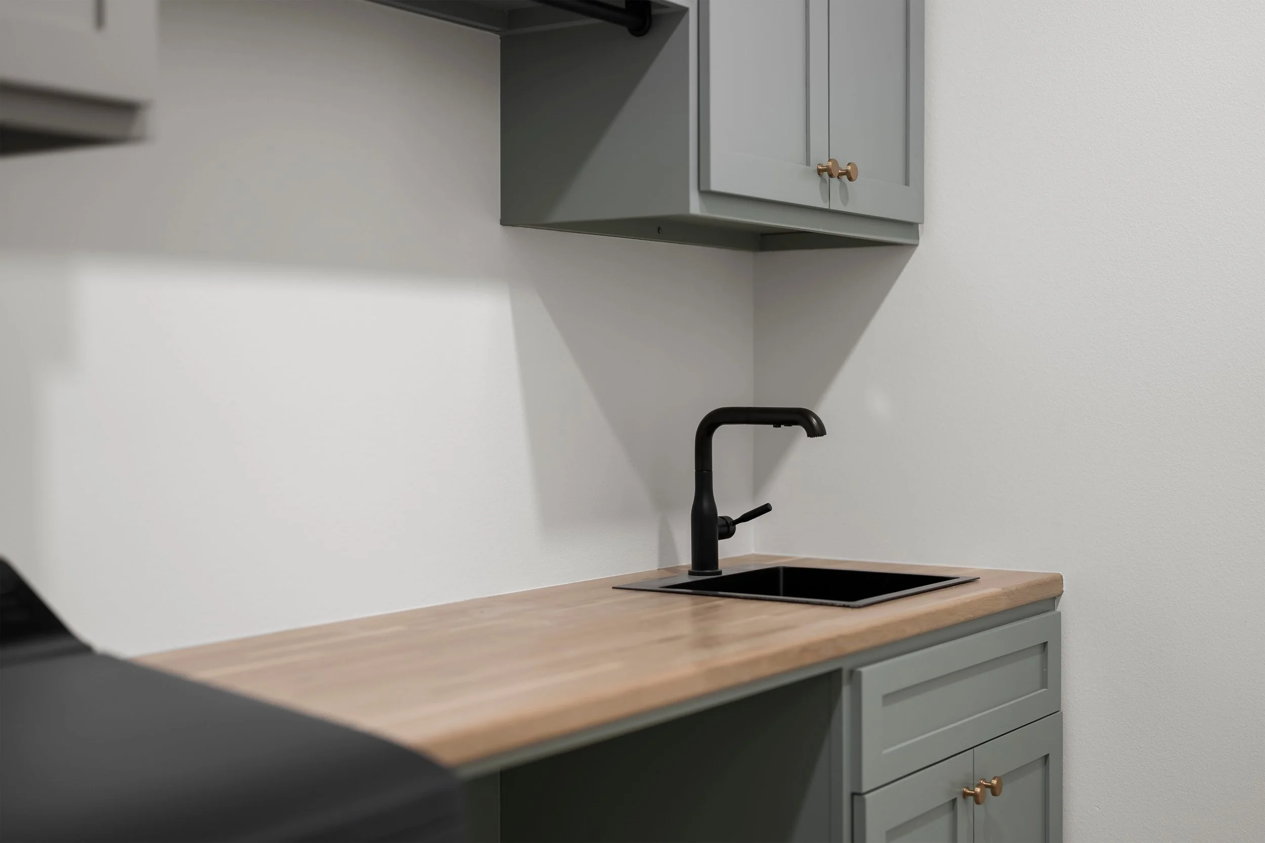 A kitchen countertop with a black faucet, a black sink, gray cabinets, and a white wall.