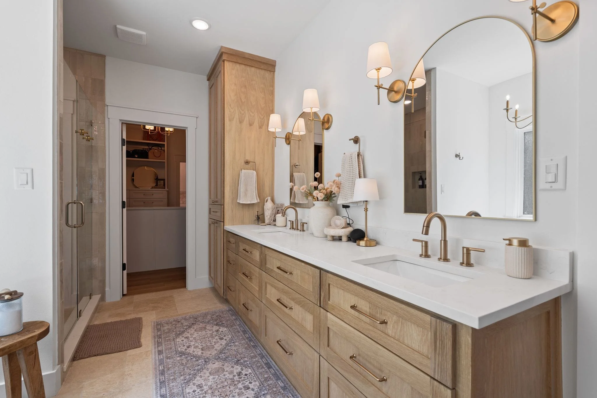 Luxury primary bathroom with double vanity, gold hardware, walk-in shower, and custom wood cabinetry.