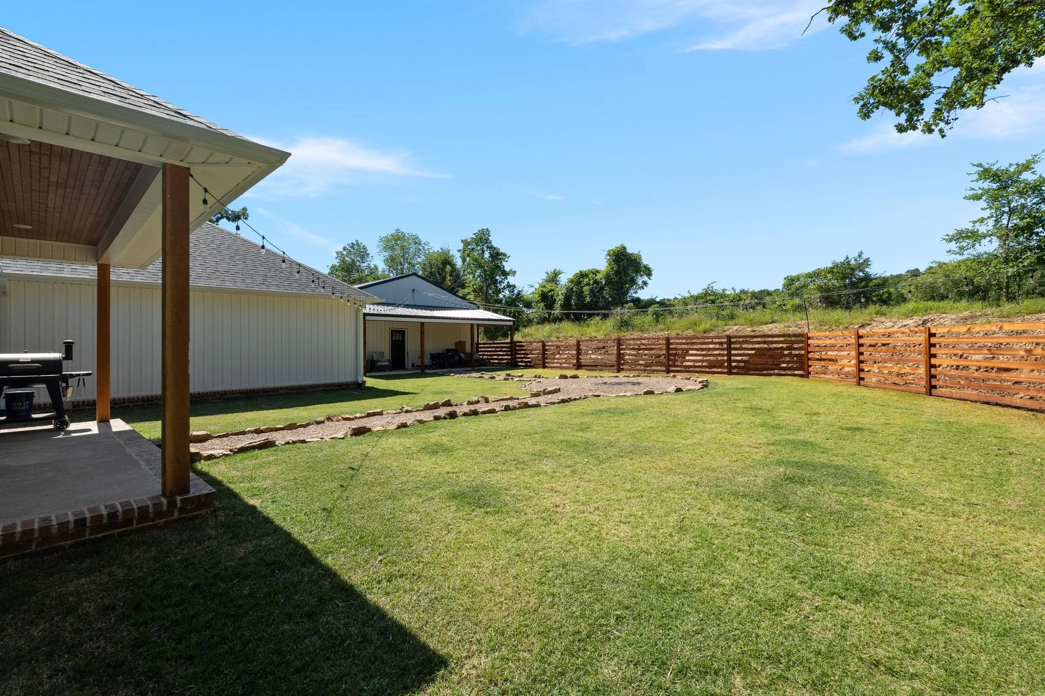 Spacious backyard with gravel fire pit, wood privacy fence, and covered patio