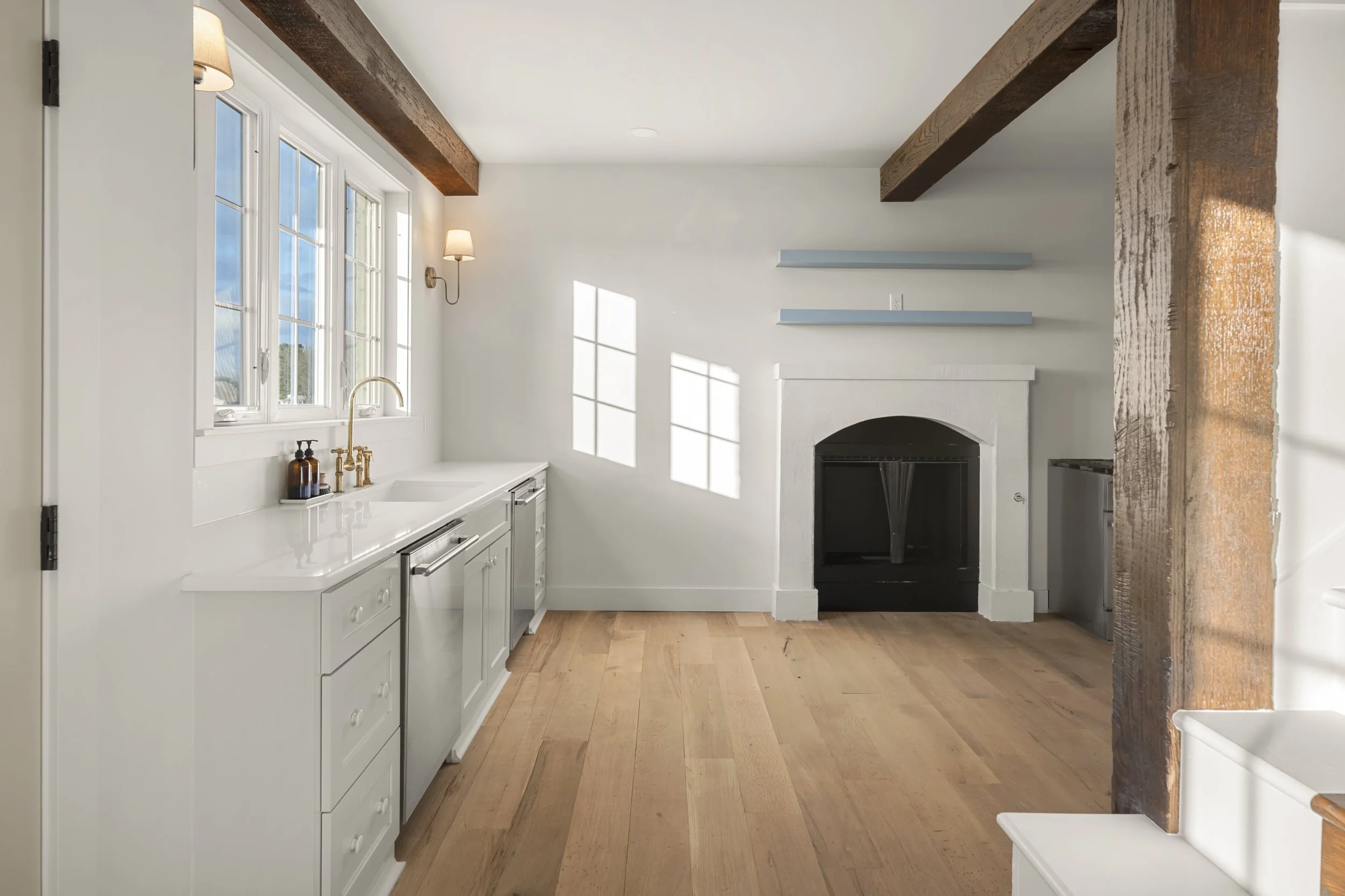 Bright kitchen with white cabinets, wooden beams, a fireplace, and natural light from multiple windows.