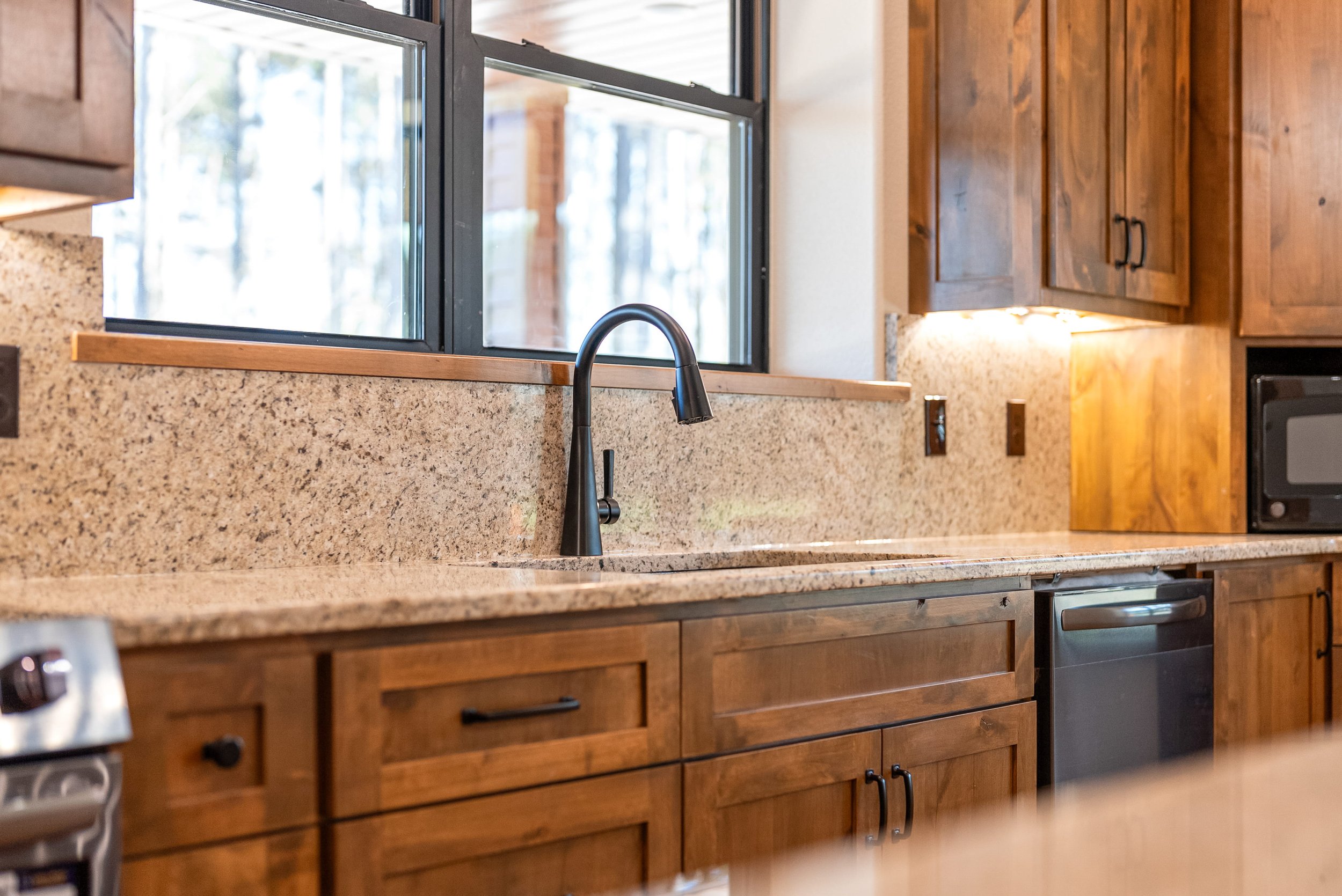 Kitchen with wooden cabinets, a granite countertop, a black faucet, a window, and a microwave.
