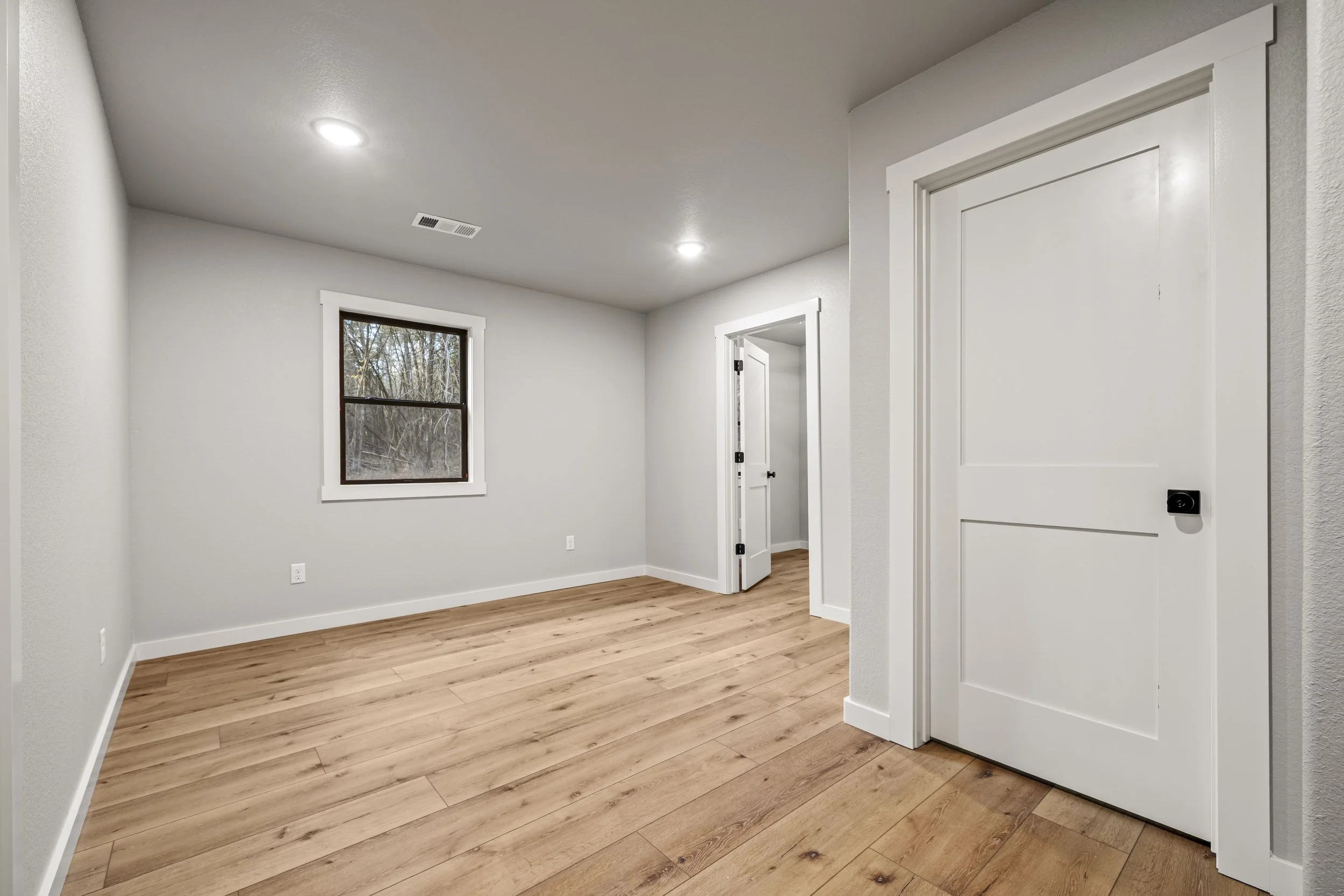 Empty room with wood floor, white walls, a window, and white trim, with two doors in the background.