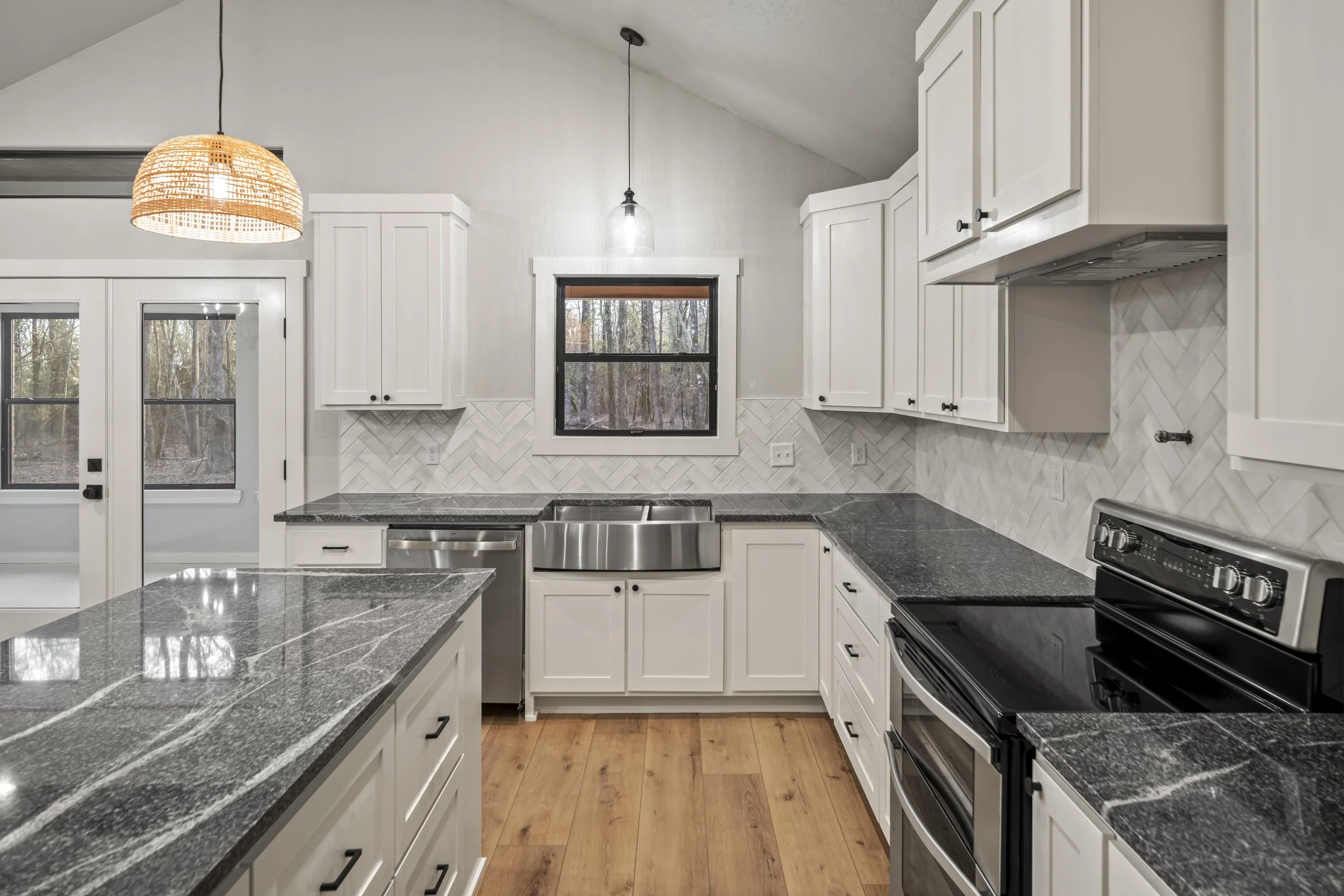 Modern kitchen with white cabinets, black and white countertops, stainless steel appliances, and a herringbone tile backsplash.