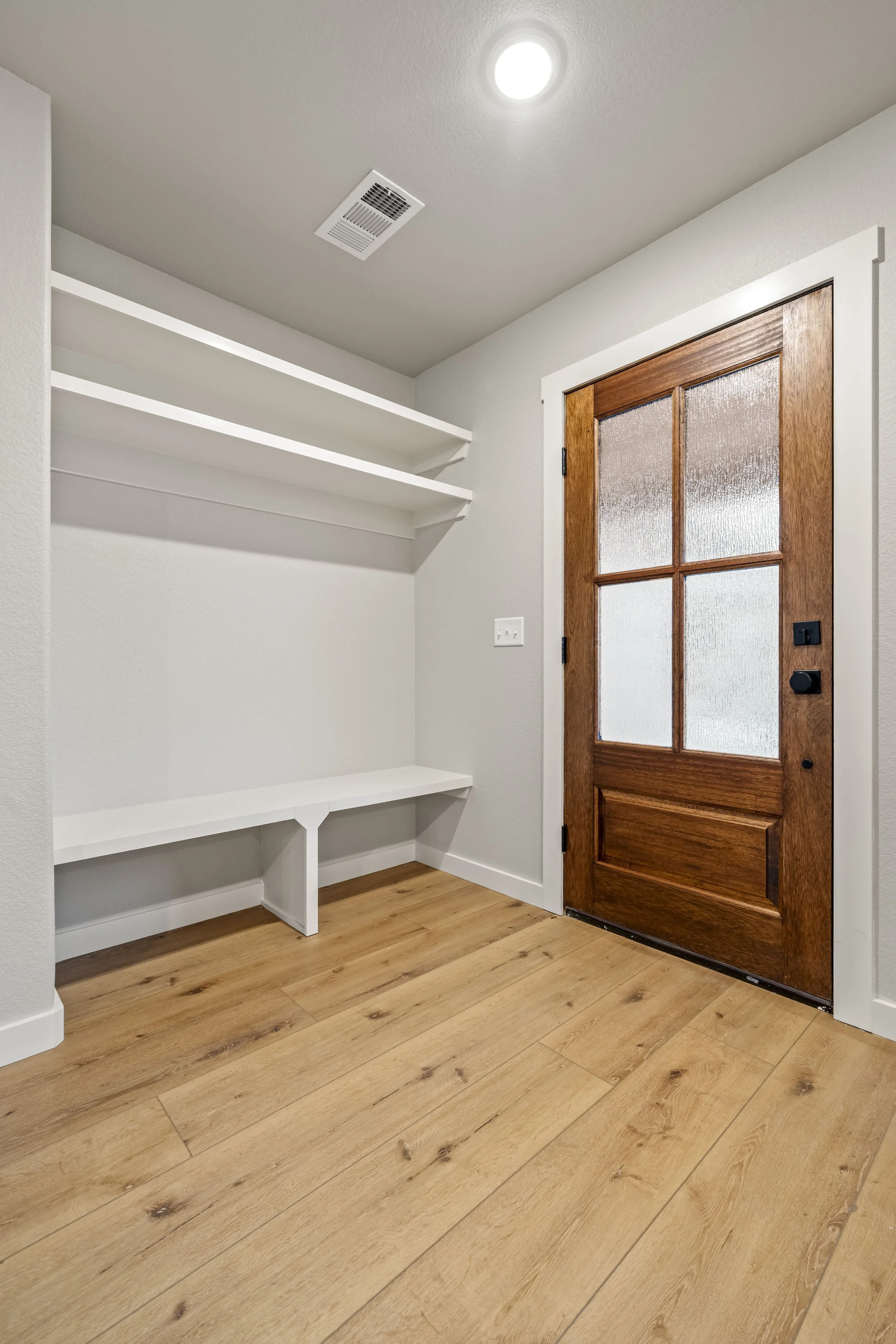 Empty room with hardwood flooring, a wooden door with frosted glass panels, white built-in shelves, and a ceiling light.