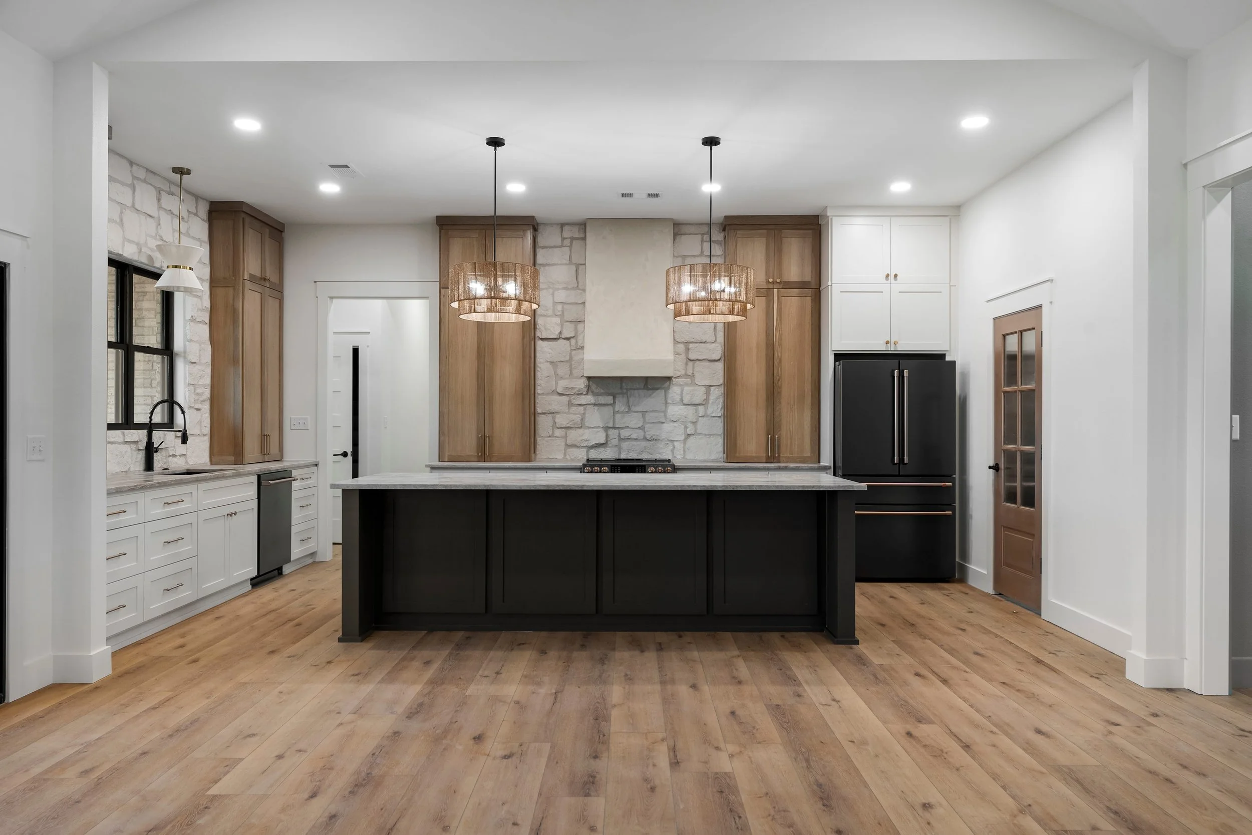 Modern kitchen with white walls, wooden cabinets, a black central island, stone backsplash, and pendant lighting.