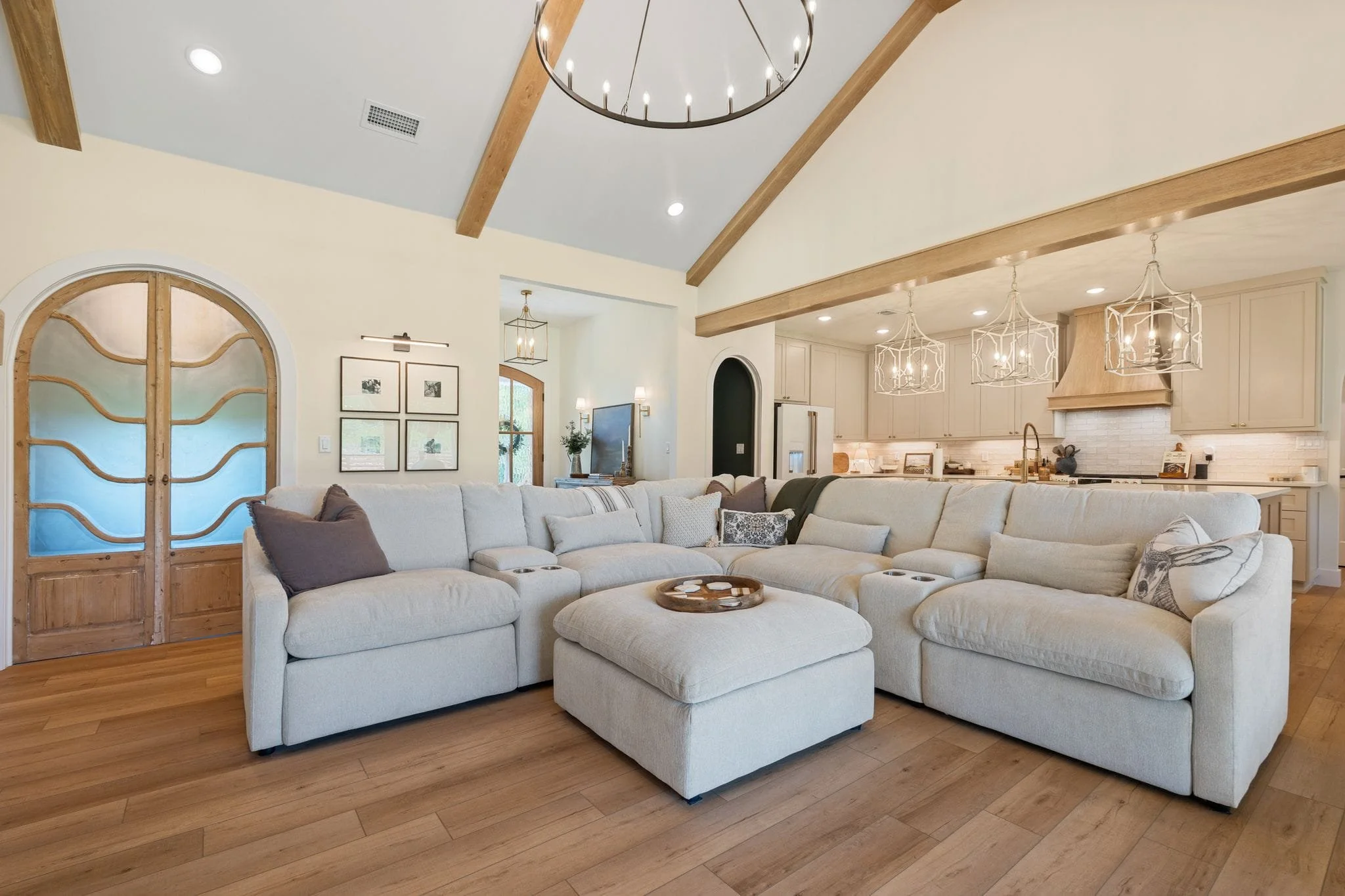 Spacious living area with oversized sectional, vaulted ceiling, exposed beams, and open kitchen connection.