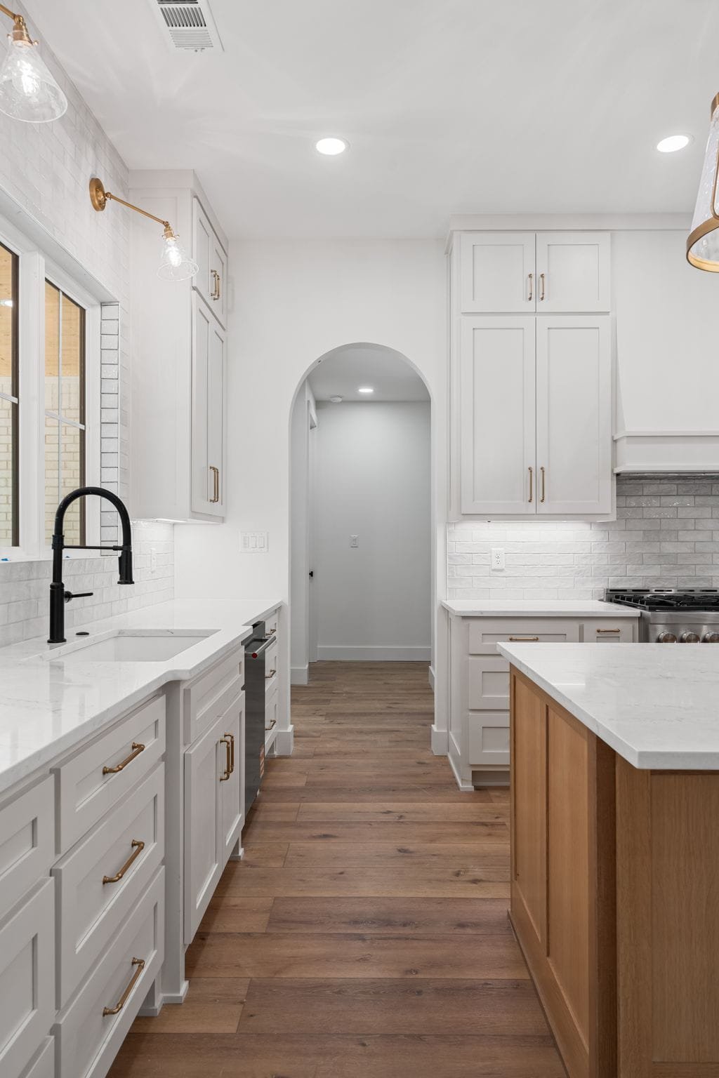 White kitchen with wooden flooring, white cabinets, black faucet, and a kitchen island with a wooden base.