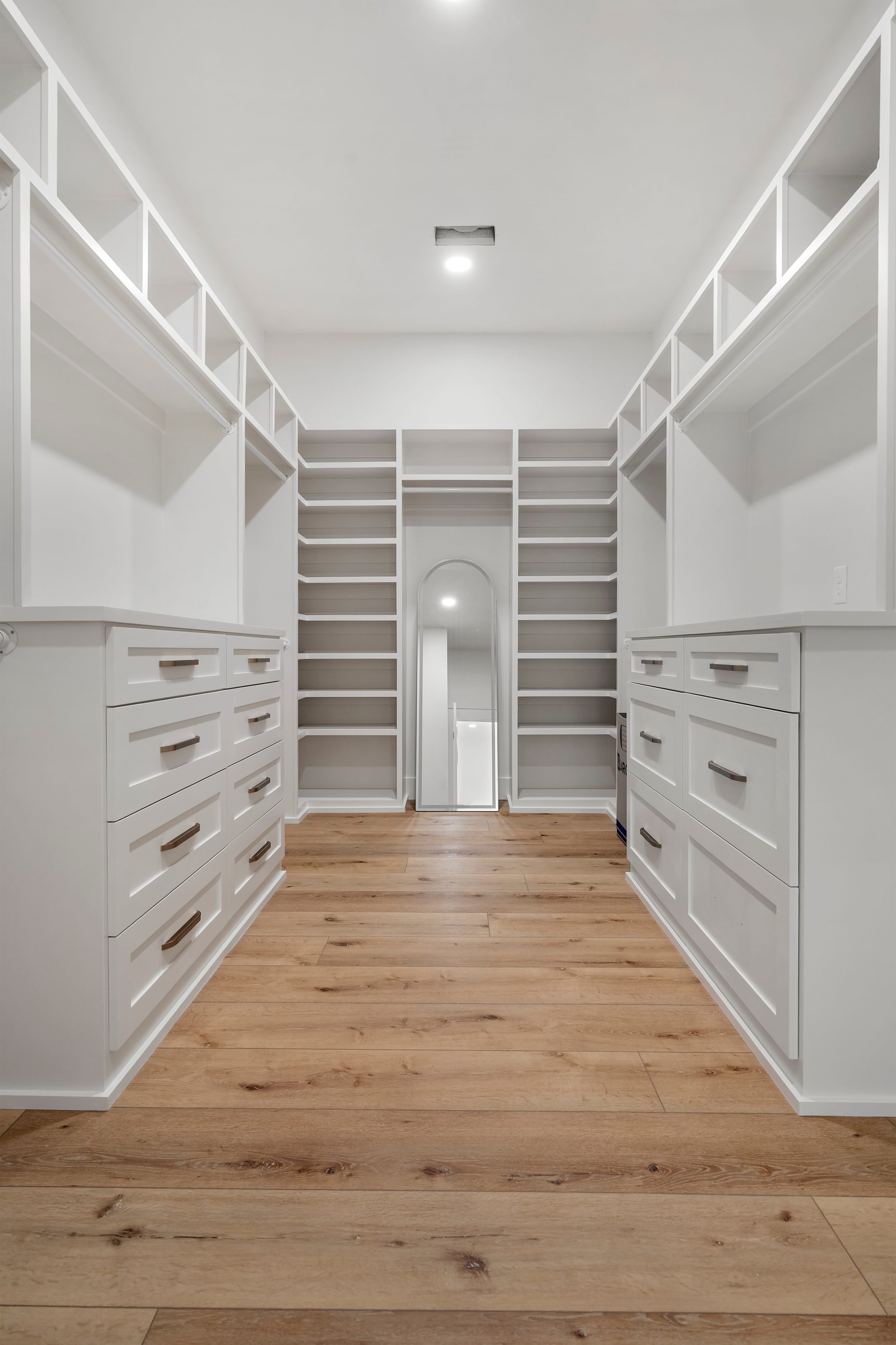 Empty walk-in closet with white shelves, drawers, and wood flooring.