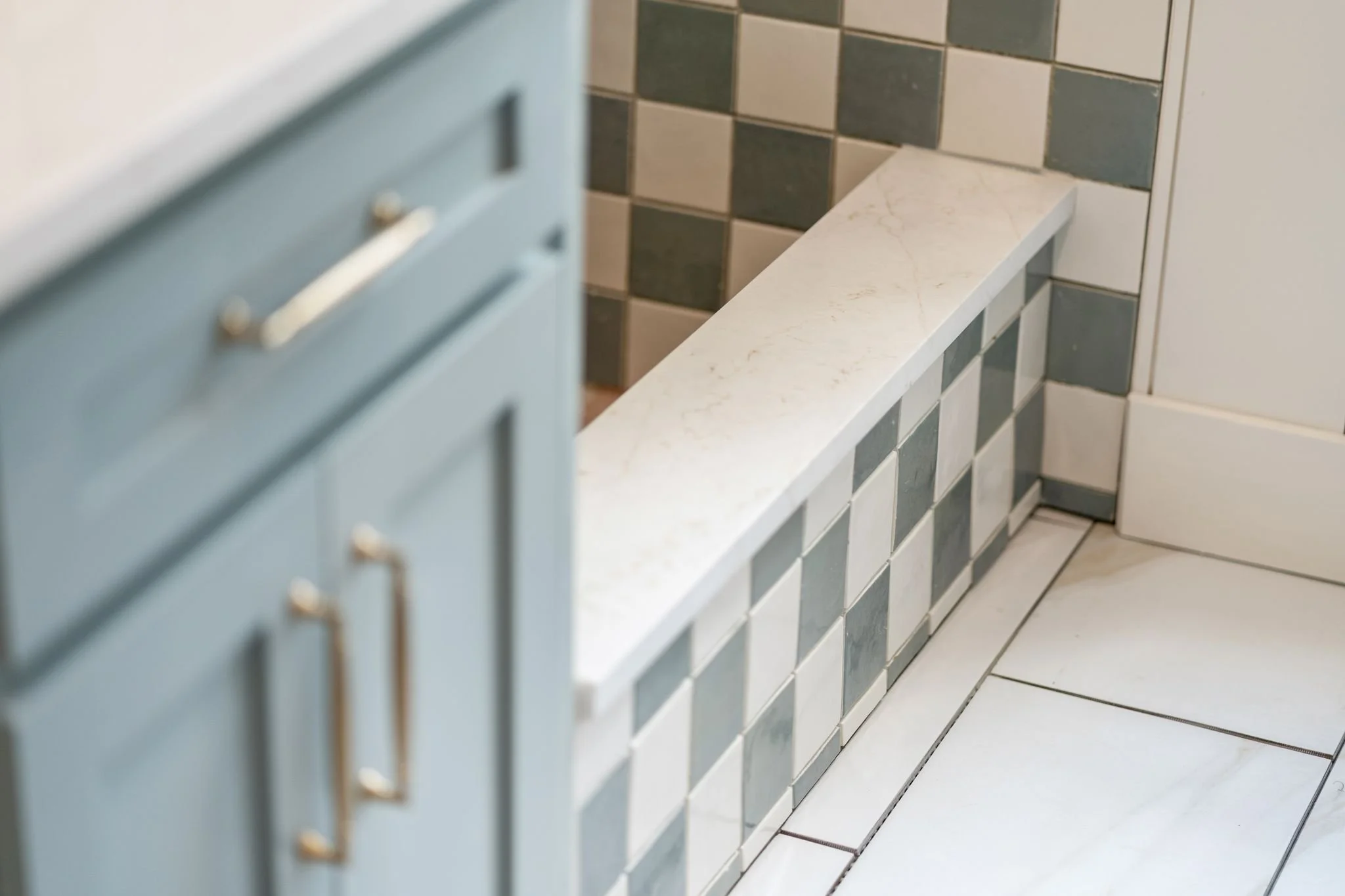 Close-up view of a tiled bathroom wall and counter with blue cabinets and white tiles on the floor.