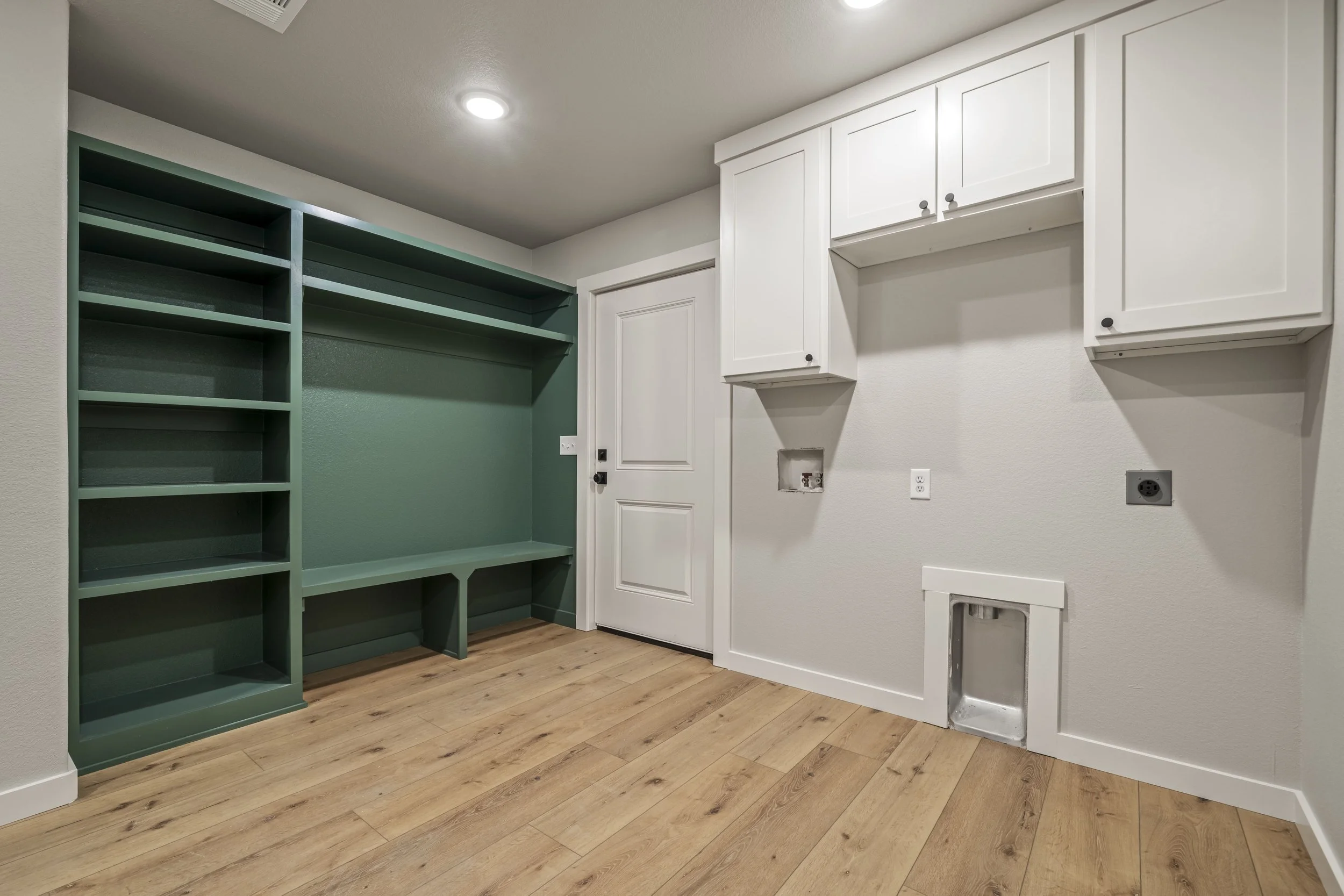 Empty laundry room with white cabinets, a built-in green bookshelf, and a dog door, with electrical outlets and a water hookup for washer and dryer.