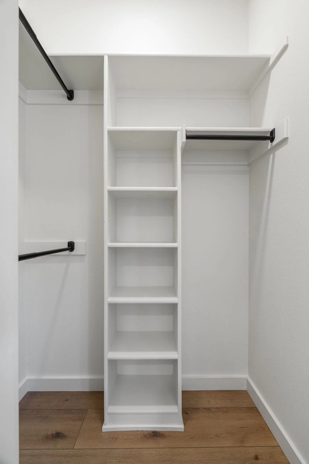 Empty white walk-in closet with shelves, hanging rods, and wood flooring.