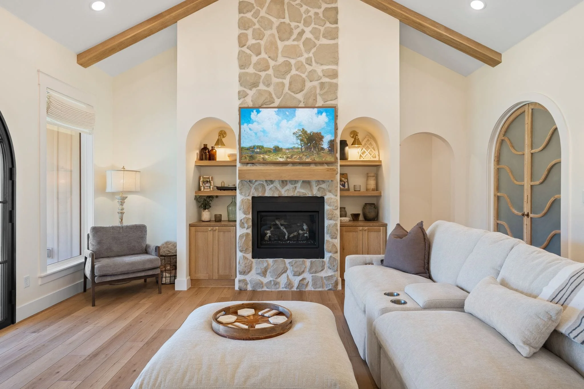 Living room with vaulted ceilings, exposed wood beams, stone fireplace, built-in shelving, and large sectional sofa.