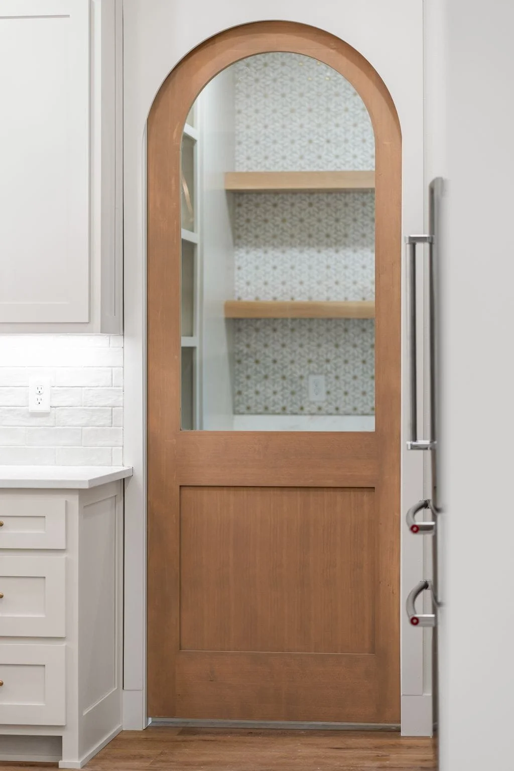Interior view of a kitchen door with a glass panel, showing two wooden shelves inside a decorative wallpapered area.