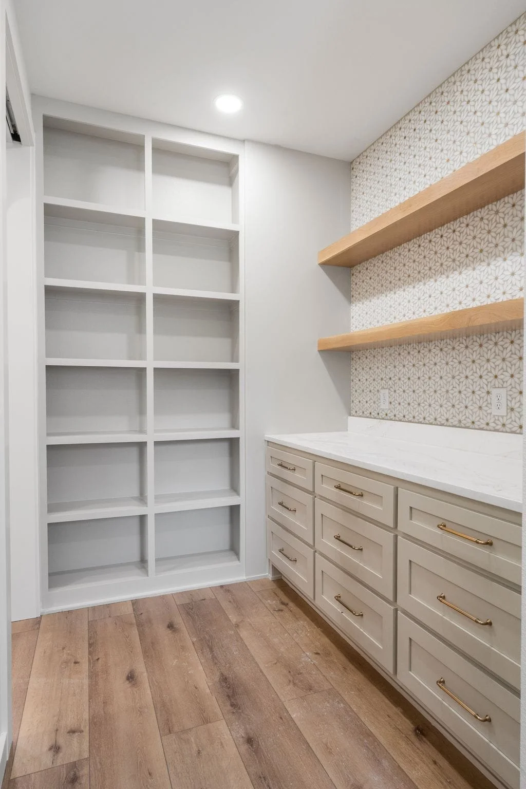 Empty white built-in shelves and drawers in a room with wood flooring and patterned wallpaper.