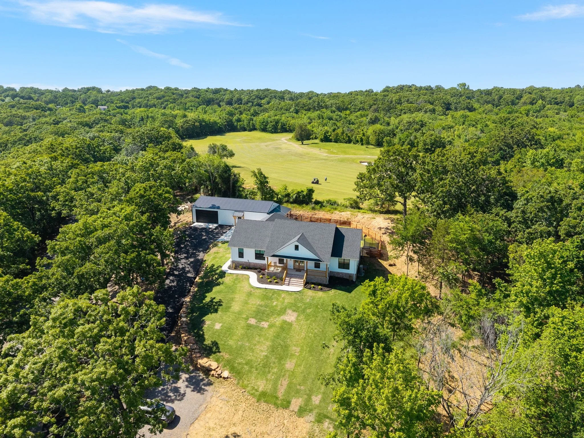 Aerial view of custom farmhouse surrounded by trees near golf course fairway