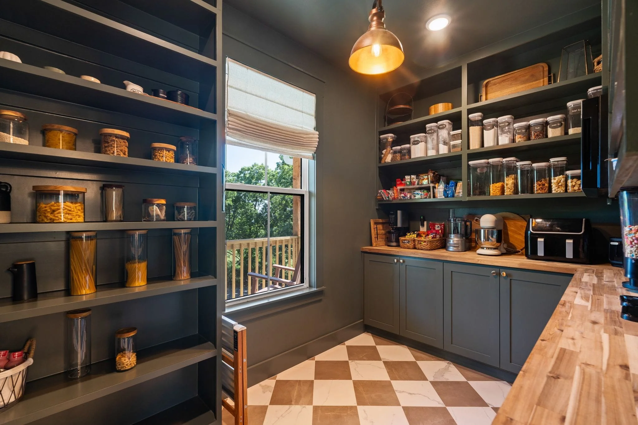 Moody walk-in pantry with dark built-ins, butcher block counters, open shelving, and checkered flooring.