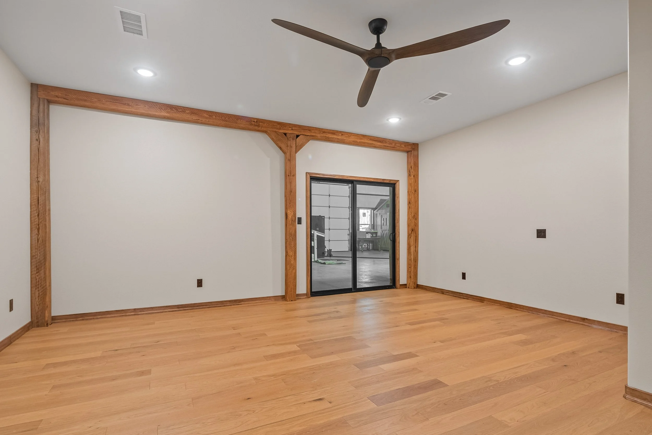 Empty room with white walls, wooden trim, hardwood floors, a ceiling fan, recessed lighting, and a sliding glass door leading outside.
